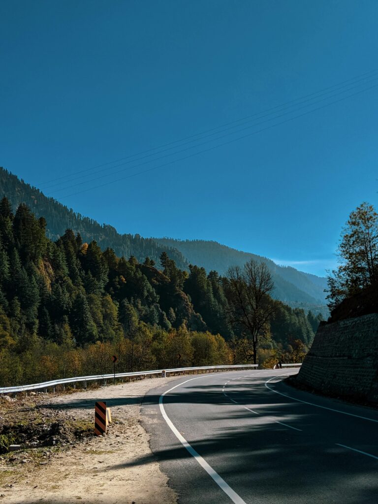 Beautiful winding road in Manali surrounded by greenery and Himalayan mountains.